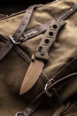 Çağdaş haki katlama bıçağı kaba bir sırt çantasının üzerinde..