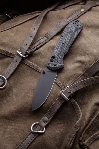 Modern folding knife on a rough canvas backpack. Melee weapons for self-defense and survival. A pocket knife on a rough dark background.