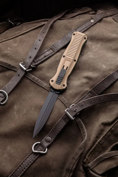 Modern folding knife on a rough canvas backpack. Melee weapons for self-defense and survival. A pocket knife on a rough dark background.