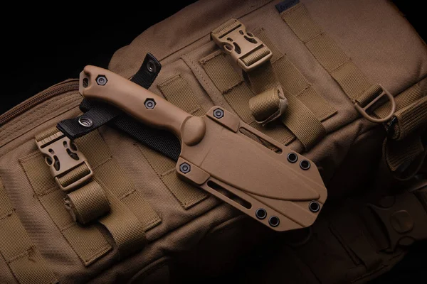 A modern military knife and a plastic sheath for it. Edged weapons lie on a desert-colored military backpack.