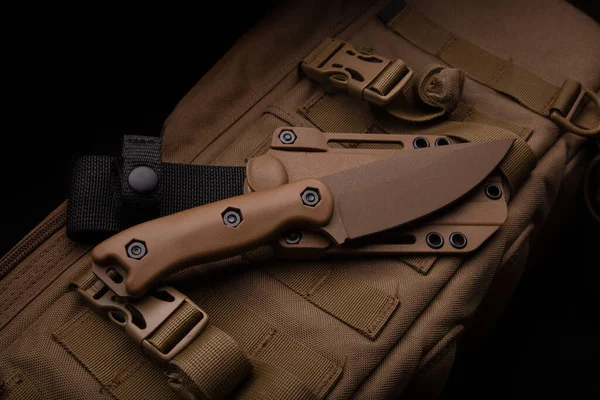 A modern military knife and a plastic sheath for it. Edged weapons lie on a desert-colored military backpack.