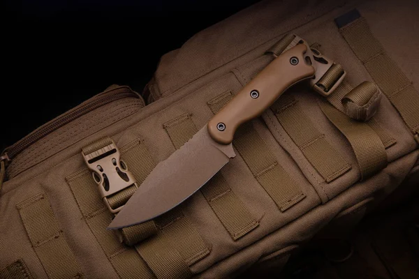 Modern bir askeri bıçak ve plastik bir kılıf. Sivri uçlu silahlar çöl rengi bir sırt çantasında yatıyor..