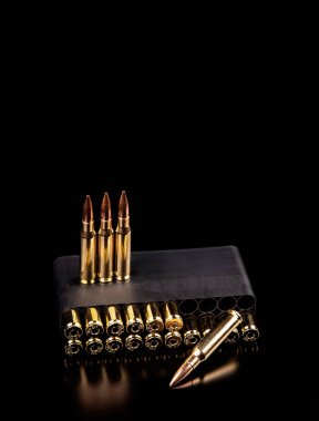 Siyah cephane kutusundaki altın kurşunlar ve karanlık, yansıtıcı yüzeyde duran üç kurşun..