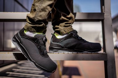 Metal bir merdivenden inen çevirmeli sistemi olan siyah ayakkabılı bir işçinin ayakları..