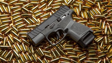 Yukarıdan bakıldığında, altın pirinç mermi yığınının üzerinde duran modern kompakt tabanca..