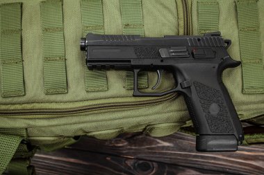 Siyah yarı otomatik tabanca zeytin yeşili taktik ağ ve koyu ahşap yüzey üzerinde dinleniyor.