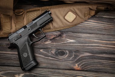 Kahverengi taktik kayışlı siyah yarı otomatik tabanca ve fotokopi alanı olan koyu renkli ahşap masa.