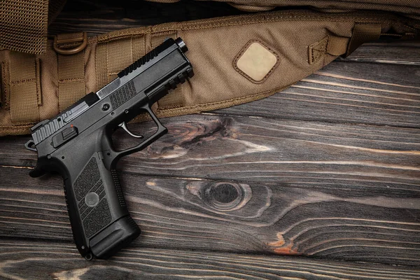 Kahverengi taktik kayışlı siyah yarı otomatik tabanca ve fotokopi alanı olan koyu renkli ahşap masa.