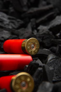 Koyu, pürüzlü kömür arka planında 12 kalibrelik üç adet av tüfeği fişeği yakın plan..