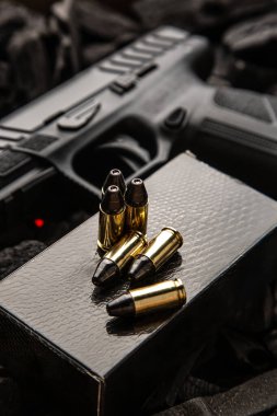 Tabanca, mühimmat kutusu ve pirinç mermiler koyu, desenli kömür arka planında.