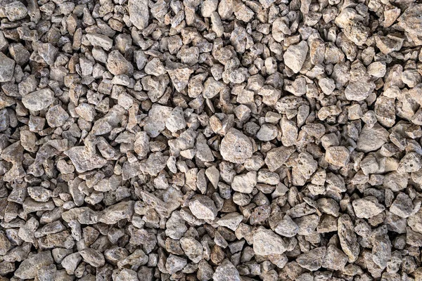 Kuru, pürüzlü, açık gri ve bej rengi ezilmiş kaya veya inşaat çakıllarının yakın çekim dokusu.