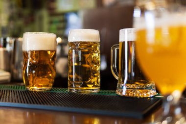 Three glasses of cold, foamy light beer sitting on a bar counter in a pub.