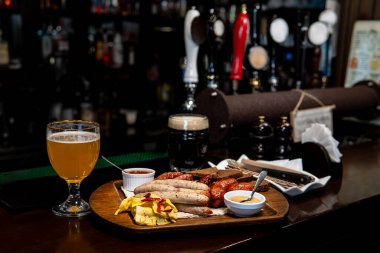 Sausages, snacks, light beer, and dark beer on a bar counter with taps in the background.