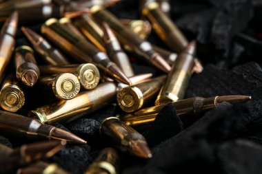 Koyu dokulu bir yüzeye yığılmış pirinç ve bakır tüfek mermilerinin yakından, dramatik bir görüntüsü..