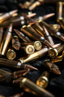 Koyu dokulu bir yüzeye yığılmış pirinç ve bakır tüfek mermilerinin yakından, dramatik bir görüntüsü..