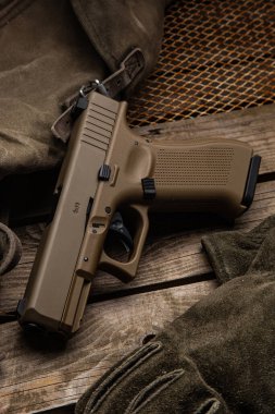 Modern askeri tarzda kahverengi bir tabanca, bir çanta ve taktik eldivenin yanındaki ahşap tahtalara dayanır..