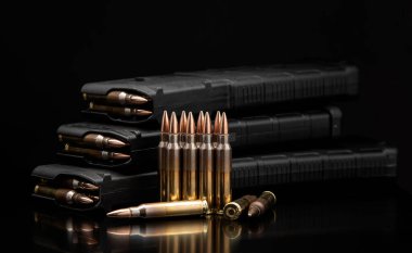 Tüfek mühimmatı ve dolu siyah polimer şarjörler koyu, yansıtıcı arka planda görüntülenir.
