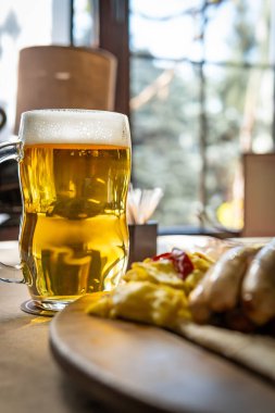 Bir kupa soğuk, köpük kafalı altın biranın yakın çekimi. Bulanık sosis tabağının yanında..