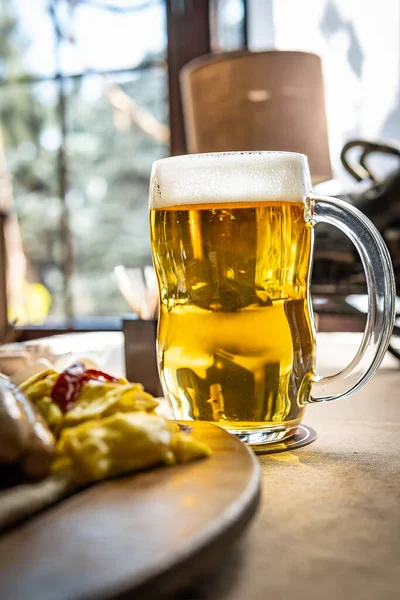 Bir kupa soğuk, köpük kafalı altın biranın yakın çekimi. Bulanık sosis tabağının yanında..