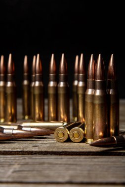 Tüfek mühimmatı siyah bir arka plana karşı koyu bir ahşap yüzeyde duruyor ve yatıyor..