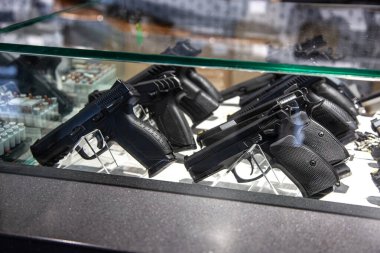 Silah dükkanında ya da fuarda cam tezgahın altında sergilenen tabancalar, siyah tabancalar..