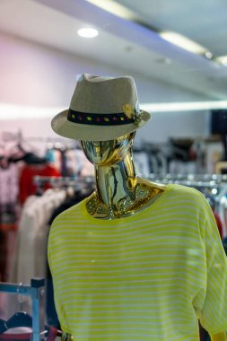 Bir butikte saman fötr şapka ve sarı çizgili gömlek giyen altın bir manken..