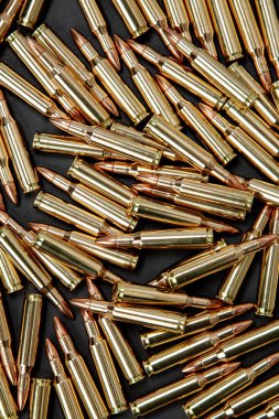 Koyu bir yüzeyde sivri uçlu mermilerle sayısız parlak pirinç tüfek fişeğinin üst görüntüsü..
