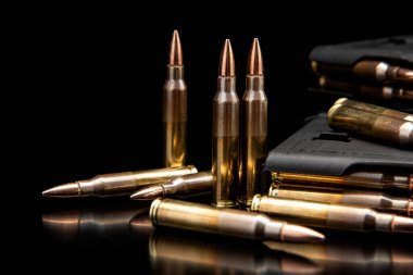 Sivri uçlu bakır mermili tüfek mermileri yansıtıcı siyah bir yüzey üzerinde duruyor..