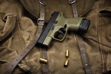 Eski bir askeri çanta üzerinde boş mermi kovanları olan zeytin yeşili kompakt tabanca..