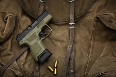 Eski bir askeri çanta üzerinde boş mermi kovanları olan zeytin yeşili kompakt tabanca..