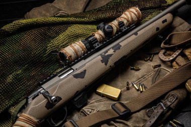 Yüksek açılı kamufle edilmiş 22 kalibre bir tüfek, dürbün, cephane ve çakmak..