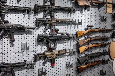 Gri tahta bir duvarda modern tüfeklerin ve klasik ahşap karabinaların çeşitli bir görüntüsü..
