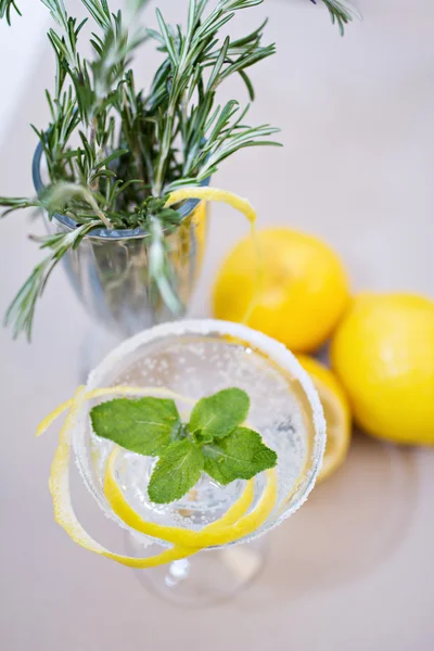 Copa de cóctel y romero con ramas de limones en una mesa —  Fotos de Stock