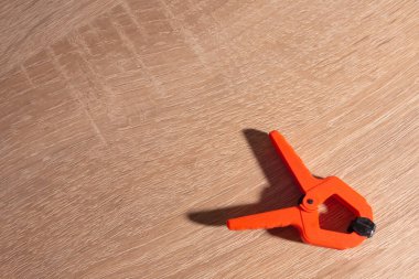 Mandallar, marangozluk kıskaçları, turuncu renkli tahta bir masanın üzerinde yatıyor.