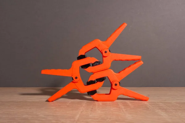 Pinces à linge, pinces à menuiserie de couleur orange reposent sur une table en bois. Une pyramide en forme de robot constitué de pinces. — Photo