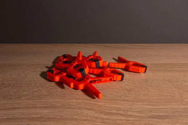 Clothespins, carpentry clamps of orange color lie on a wooden table. — Stock Photo, Image