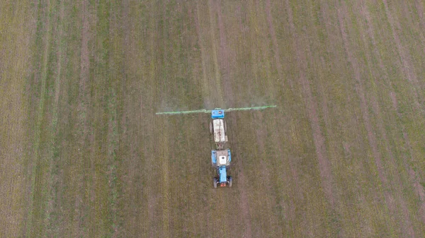 Spring field work. Early shoots. A tractor with attachments sprays fertilizer onto the field