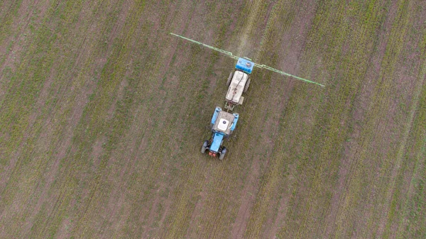 Spring field work. Early shoots. A tractor with attachments sprays fertilizer onto the field