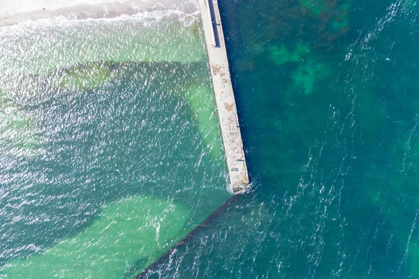 Sandy beach, concrete pier, clear sea water. Helicopter view