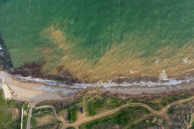 Dik deniz kıyısı ve sörf. Deniz suyu, kum üstüne fırtına ve yosun ile çamurlu. Hava görünümü