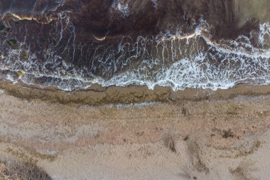 Dik deniz kıyısı ve sörf. Deniz suyu, kum üstüne fırtına ve yosun ile çamurlu. Hava görünümü