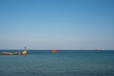 Turuncu bir pilot botu, geminin limana kadar eşlik etmesi için dış yola çıkıyor.
