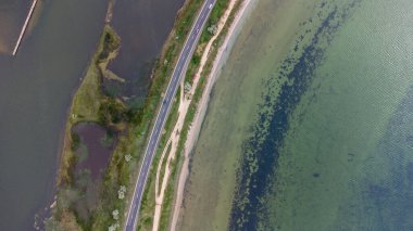 Deniz ve haliçler arasında dar bir tükürük boyunca uzanan bir otoyol. Arabalar yolda. Hava görünümü.
