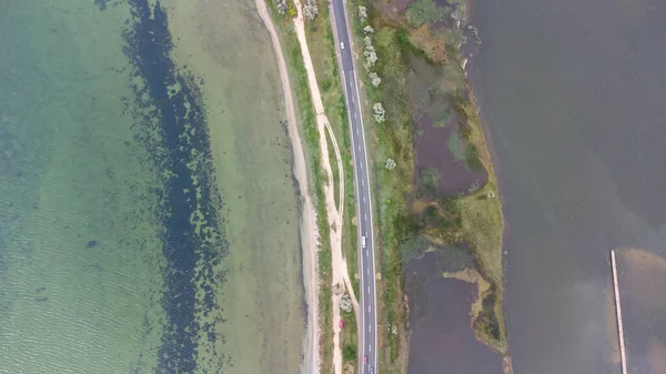 Uma estrada que corre ao longo de uma estreita saliva entre o mar e o estuário. Carros na estrada. Vista aérea. — Fotografia de Stock