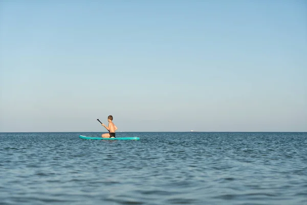 Een 12-jarige jongen leert op een SUP-plank te staan in de zee bij de kust. — Stockfoto