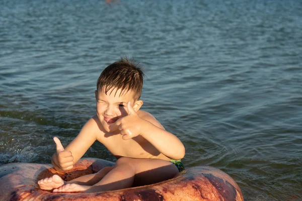 Un niño de 6 años nada en un anillo inflable en el mar cerca de la orilla. — Foto de Stock