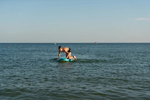 Een 12-jarige jongen leert op een SUP-plank te staan in de zee bij de kust. — Stockfoto