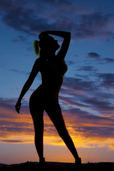Silhuetten av en kvinna i en bikini höfter till sidan handen över huvud — Stockfoto