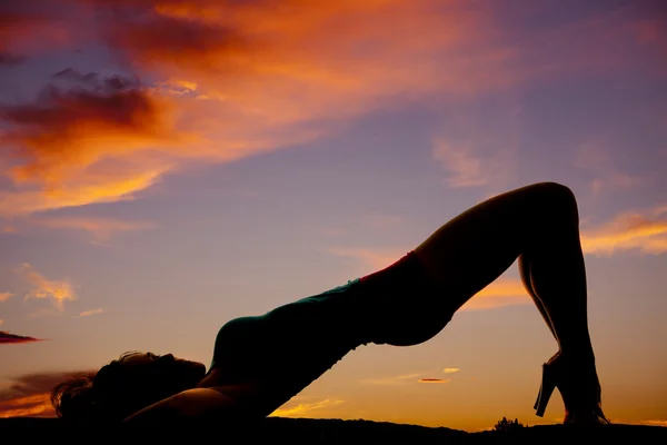 Silhouette einer Frau im Sonnenuntergang, die sich mit Po und Knie zurücklehnt — Stockfoto