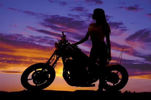 Silueta de una mujer de pie junto a una motocicleta mirando hacia adelante — Foto de Stock